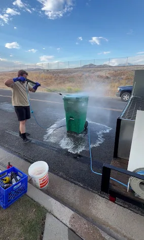 Rad Cans technician pressure washing a green trash can at the curb with hot water in Utah
